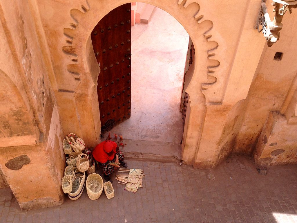 Baskets and slippers for sale beside a painted doorway in the Marrakech medina.